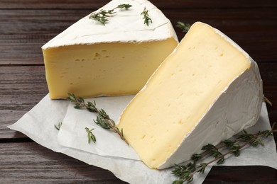 Photo of Pieces of tasty camembert cheese and thyme on wooden table, closeup