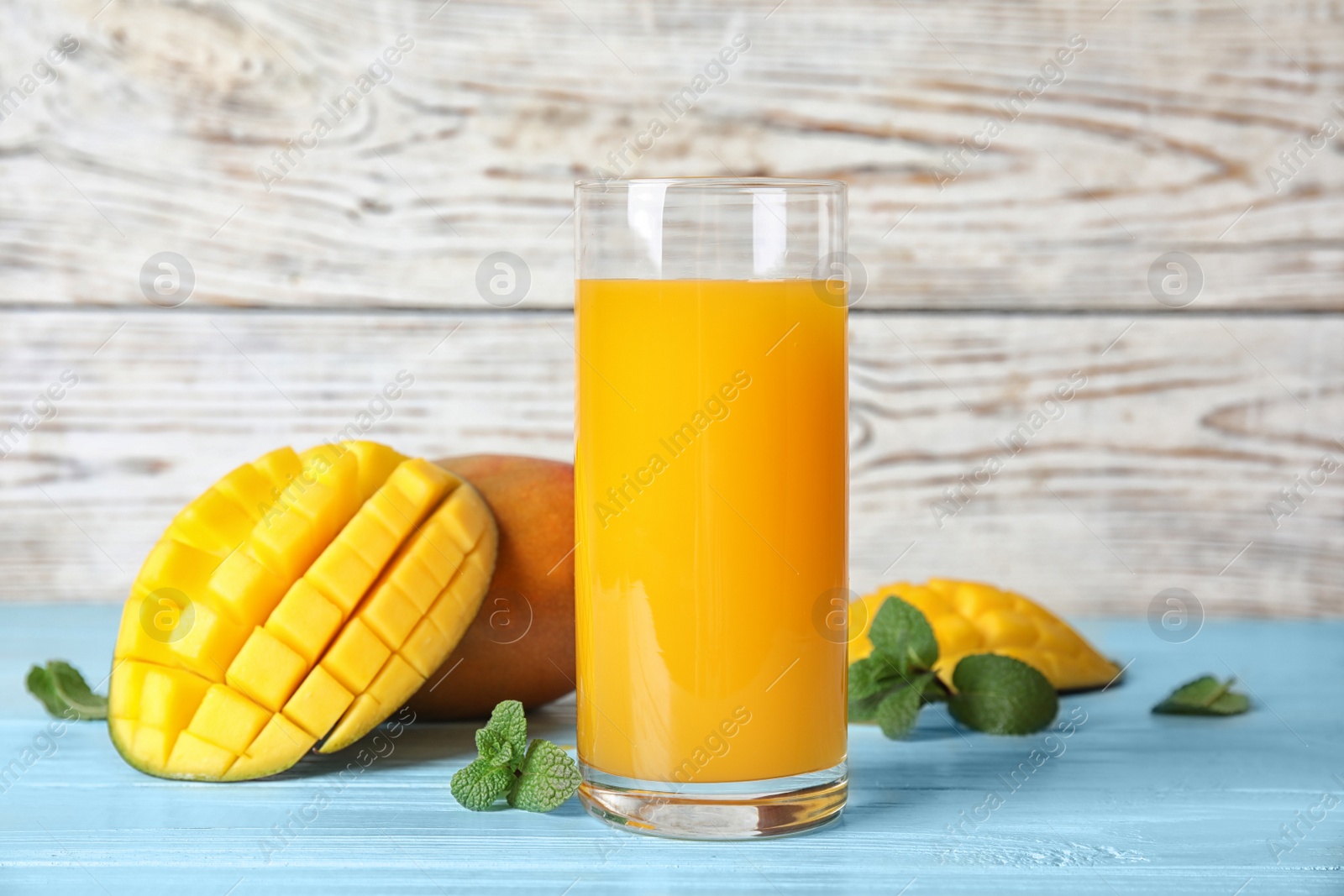 Photo of Glass with fresh mango juice and tasty fruits on wooden table