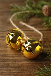 Photo of Golden sleigh bells and fir branch on wooden table, closeup