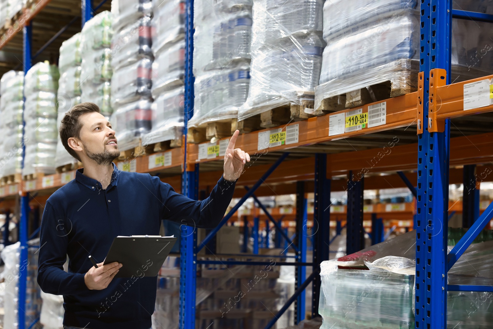 Photo of Happy manager holding clipboard in warehouse with lots of products