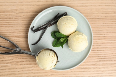 Plate with delicious vanilla ice cream, mint, pods and scoop on wooden table, flat lay