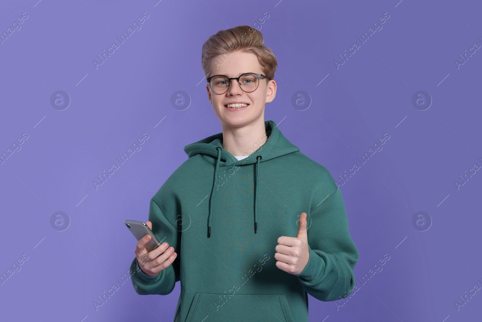 Photo of Teenage boy with smartphone showing thumb up on purple background