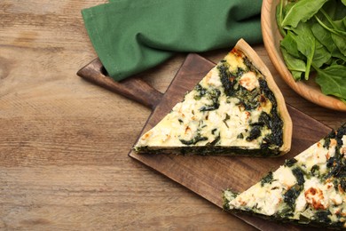 Pieces of delicious homemade quiche and fresh spinach leaves on wooden table, flat lay. Space for text