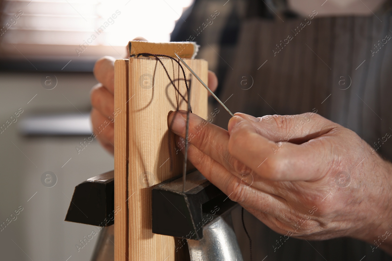 Photo of Man sewing piece of leather in workshop, closeup