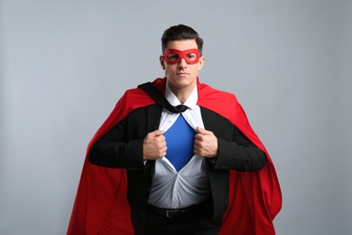 Businessman in superhero cape and mask taking suit off on grey background