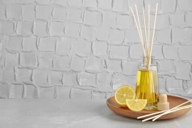 Photo of Plate with aromatic reed freshener and lemon on table against textured wall. Space for text