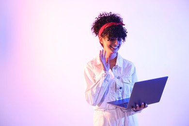 Photo of Beautiful young woman with laptop on color background in neon lights. Space for text