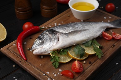Photo of Fresh raw dorado fish with lemon, spices and tomatoes on black wooden table