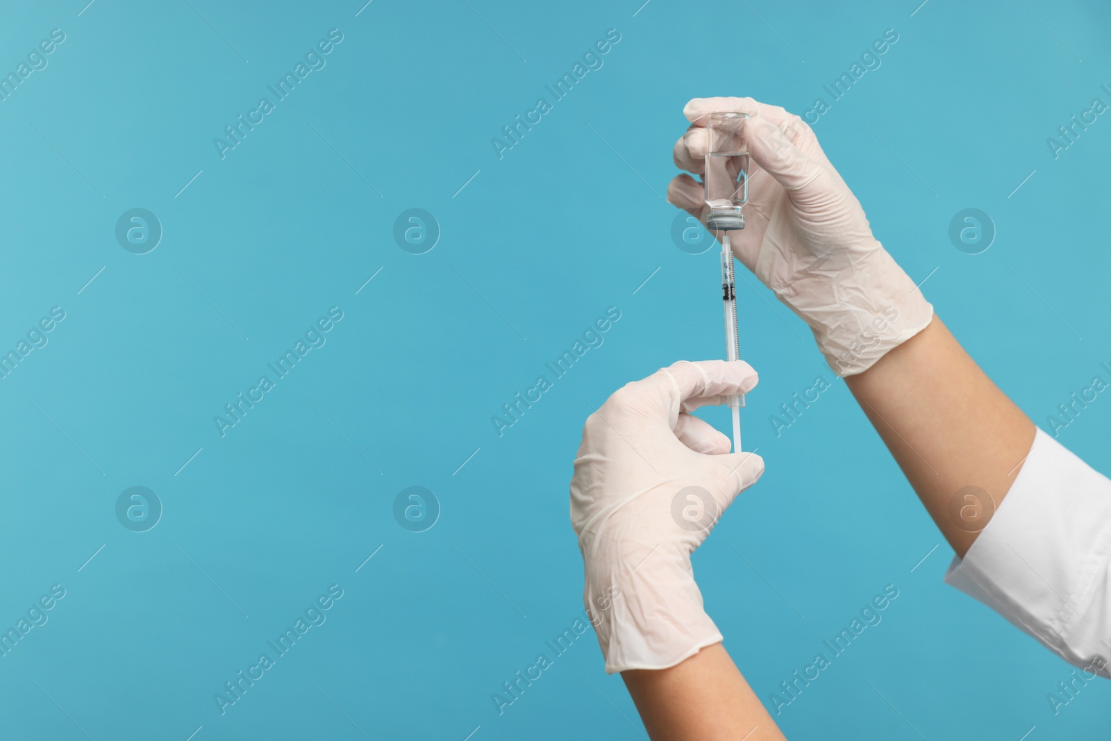 Photo of Doctor filling syringe with medication from glass vial on light blue background, closeup. Space for text