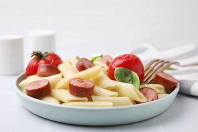 Tasty pasta with smoked sausage, tomatoes and basil on white table, closeup. Space for text