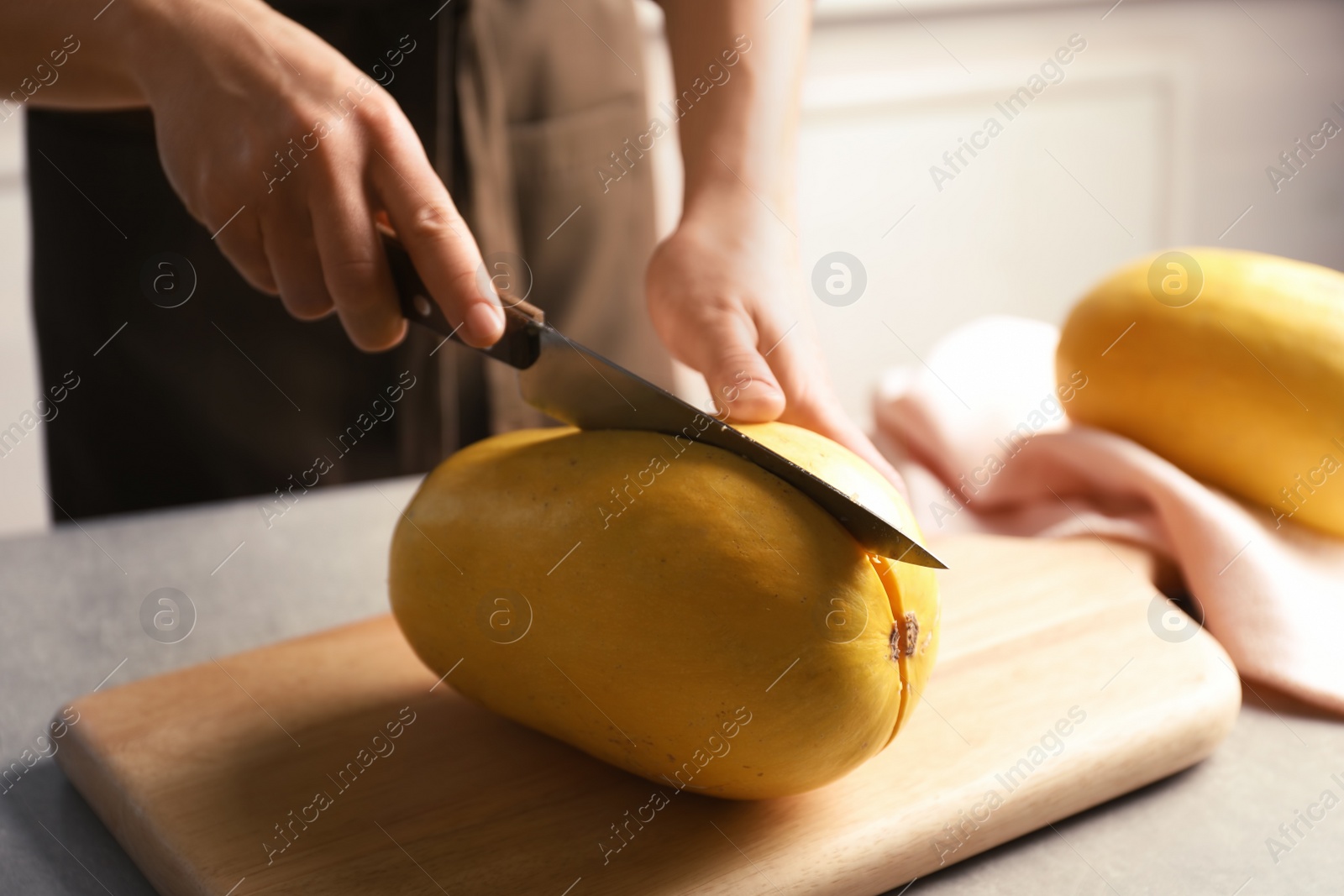 Photo of Woman cutting spaghetti squash on table in kitchen, closeup