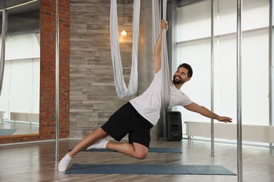 Man with hammock practicing fly yoga in studio
