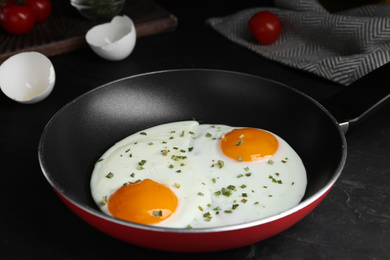 Photo of Tasty cooked eggs with herbs in frying pan on black table, closeup