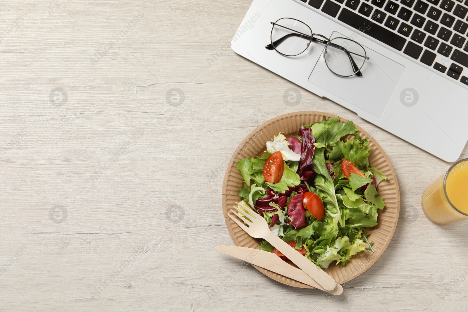 Photo of Fresh vegetable salad, glass of juice and laptop on white wooden table at workplace, flat lay with space for text. Business lunch