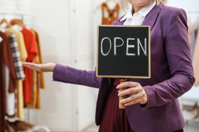 Female business owner holding OPEN sign in boutique, closeup