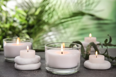 Photo of Burning candles and spa stones on grey table against blurred green background, space for text