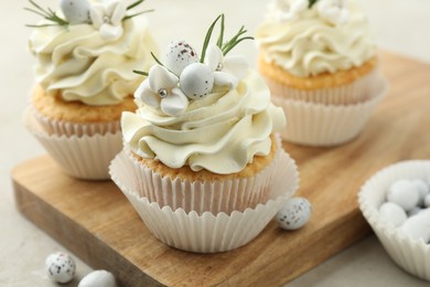 Photo of Tasty Easter cupcakes with vanilla cream and candies on gray table, closeup