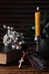 Photo of Rosary beads, Bible, burning candle and willow branches on wooden table, closeup