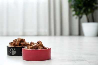 Photo of Wet pet food in feeding bowls on floor indoors, space for text