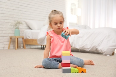 Photo of Cute child playing with building blocks on floor at home