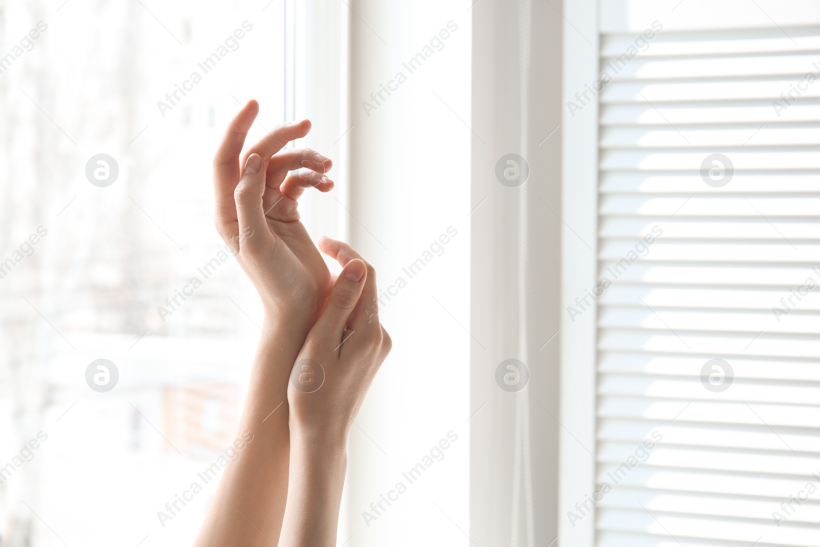 Photo of Young woman against window. Focus on hands moisturized with cream