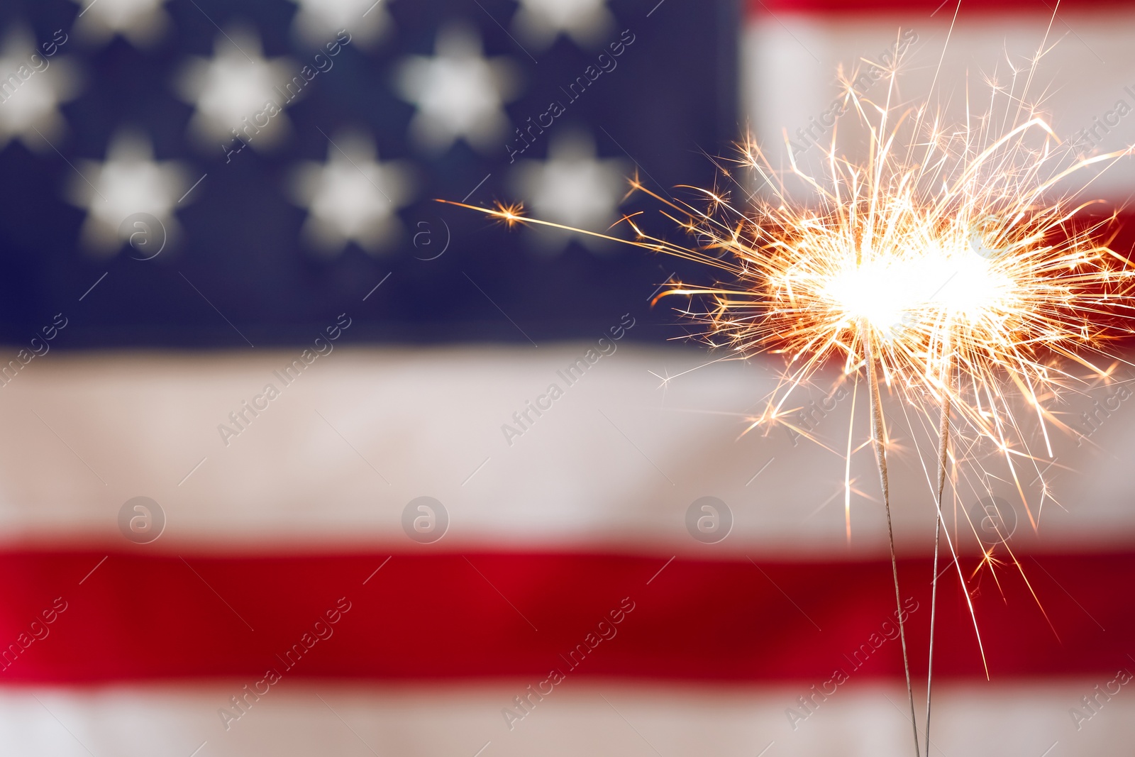 Photo of Bright burning sparklers against American flag, closeup. Space for text