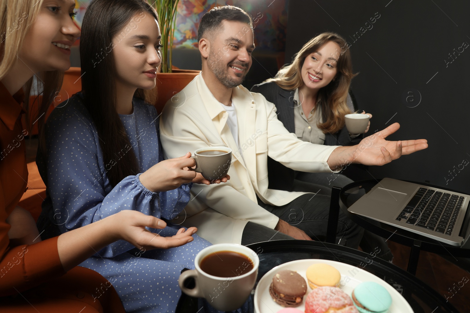 Photo of People with coffee, macarons and laptop spending time together in cafe