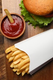 Photo of French fries, tasty burger and sauce on wooden table, flat lay