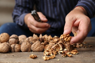 Man cracking walnuts at wooden table, closeup