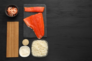 Photo of Making sushi rolls. Flat lay composition with fresh salmon and other ingredients on black wooden table. Space for text