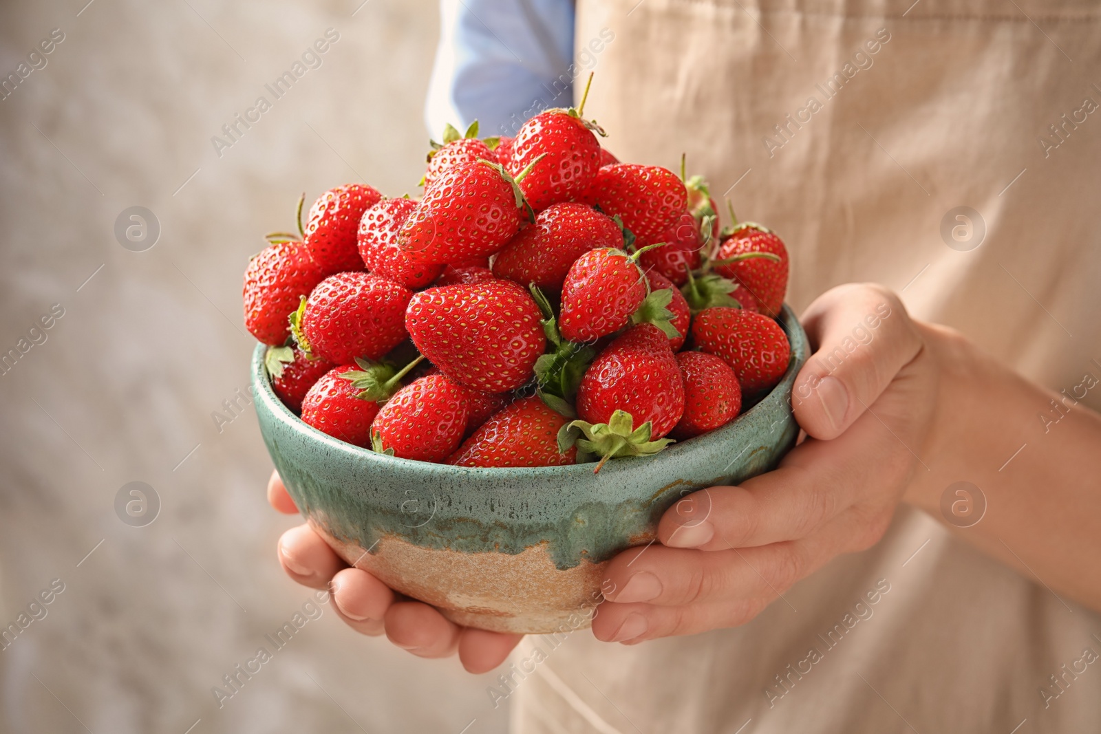 Photo of Young woman holding bowl with fresh ripe strawberries on grey background, closeup