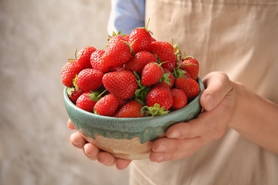 Photo of Young woman holding bowl with fresh ripe strawberries on grey background, closeup