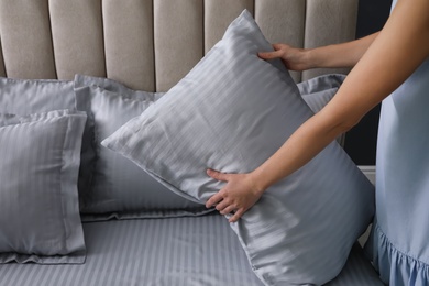 Photo of Woman putting soft pillow on bed, closeup