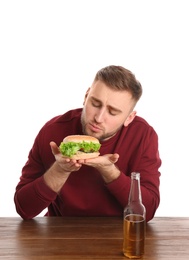 Young man with tasty burger and beer at table on white background