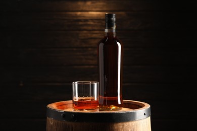 Photo of Glass and bottle of tasty whiskey on wooden barrel