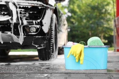 Car cleaning supplies and auto covered with foam outdoors. Space for text