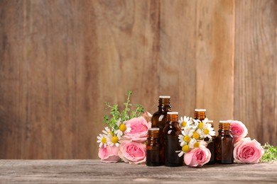 Bottles with essential oils, thyme and flowers on wooden table. Space for text