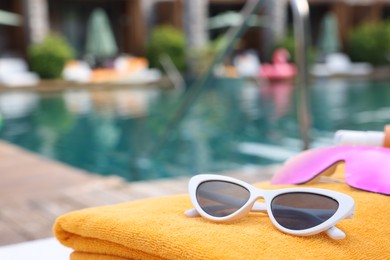 Photo of Beach towel and sunglasses near outdoor swimming pool at luxury resort, closeup. Space for text