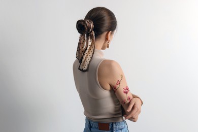 Image of Young woman with tattoo of beautiful sakura tree branch on light grey background, back view
