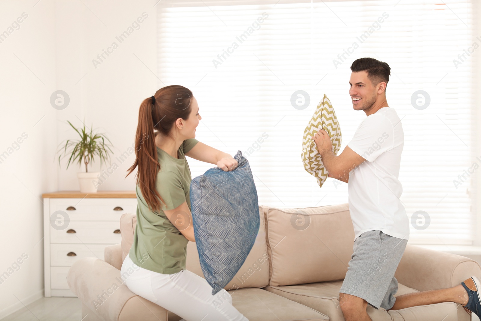 Photo of Happy couple having pillow fight in living room