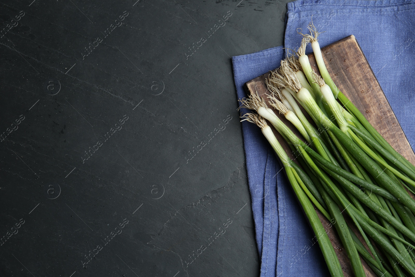 Photo of Fresh green spring onions on black table, flat lay. Space for text