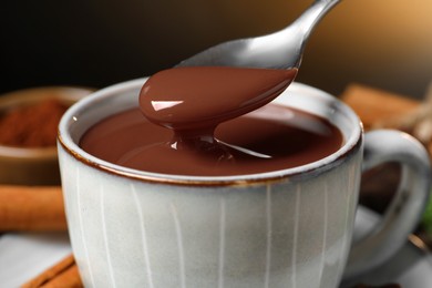 Photo of Spoon with yummy hot chocolate over cup, closeup