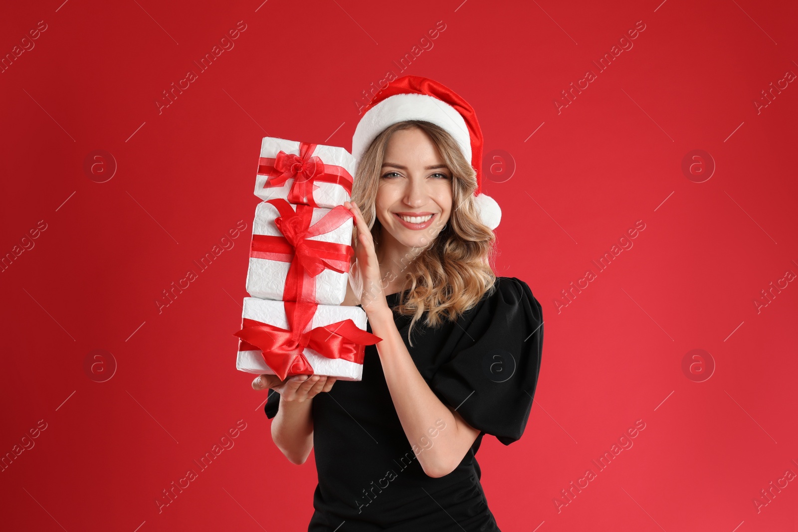 Photo of Beautiful young woman in Santa hat with Christmas presents on red background