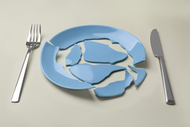 Pieces of broken ceramic plate and cutlery on beige background