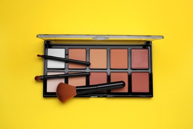 Photo of Colorful contouring palette with brushes on yellow background, top view. Professional cosmetic product