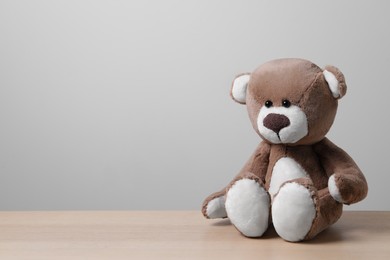 Photo of Cute teddy bear on wooden table near light wall, space for text