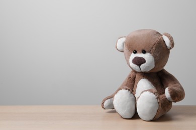 Cute teddy bear on wooden table near light wall, space for text