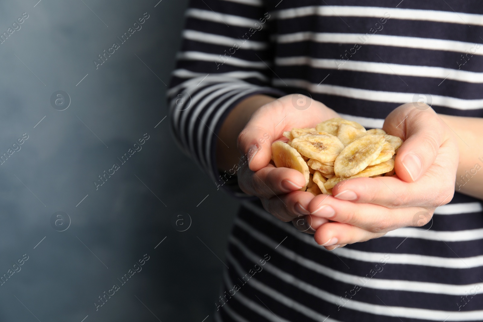 Photo of Woman holding handful of sweet banana slices on color background, closeup with space for text. Dried fruit as healthy snack