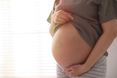 Photo of Young pregnant woman near window indoors, closeup. Space for text