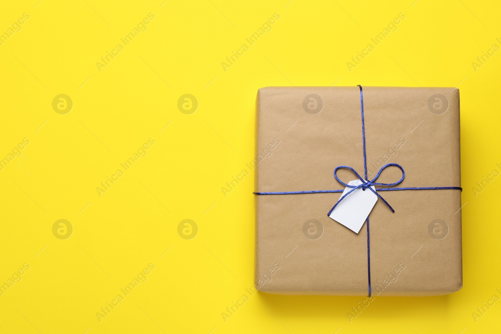 Photo of Parcel wrapped in kraft paper with tag on yellow background, top view. Space for text